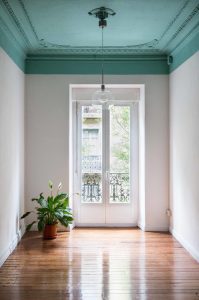 Sala con puerta a balcon en blanco. Suelo de parquet. Techo y molduras pintadas en verde.